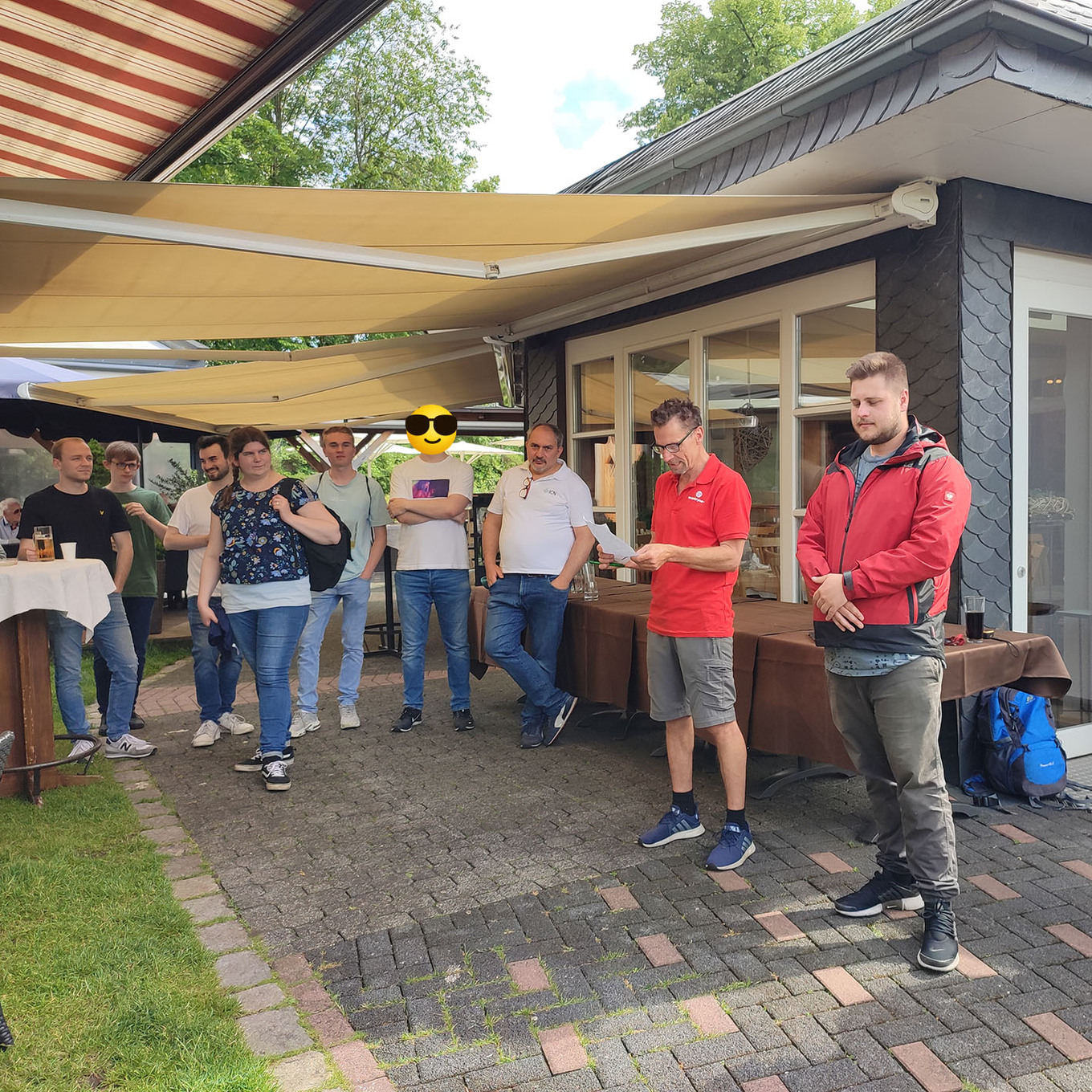 Gruppe von Männern, die draußen unter einem Vordach vor einem Gebäude stehen und sich unterhalten 