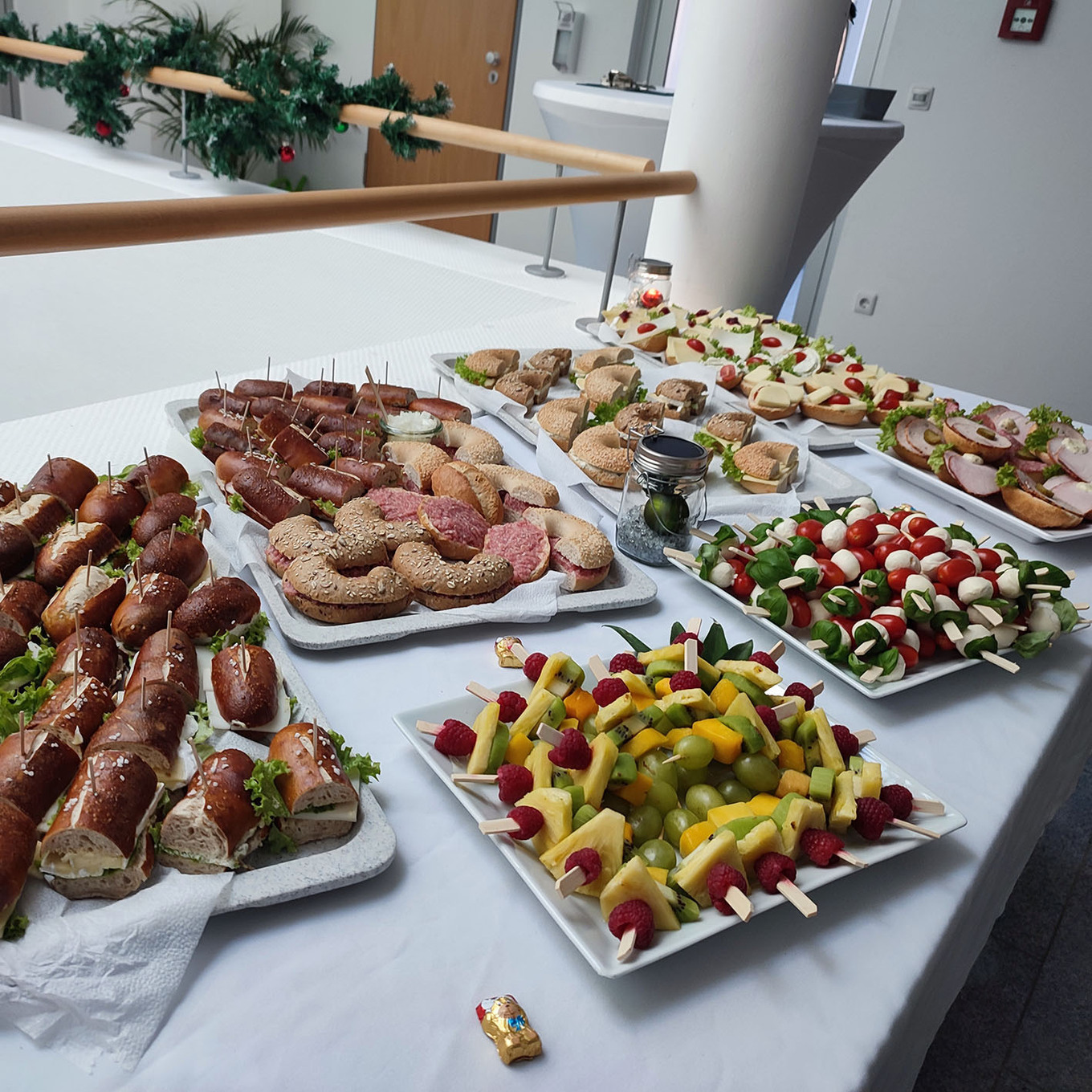 Buffet mit verschiedenen Platten voller Speisen, darunter herzhafte Häppchen, Obstspieße und kleine Gebäcke 