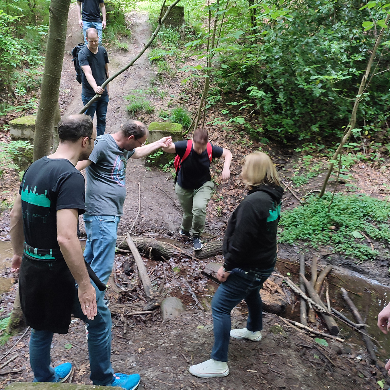 Gruppe von Wanderern. die sich auf einem rutschigen, schlammigen Waldweg gegenseitig beim Aufstieg helfen 