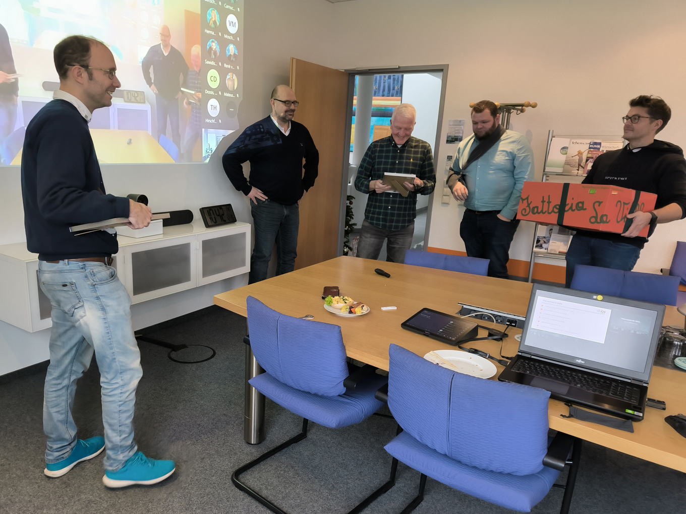 5 Männer in einem Konferenzraum, einer von ihnen hält eine Präsentation, während die anderen ihm zuhören