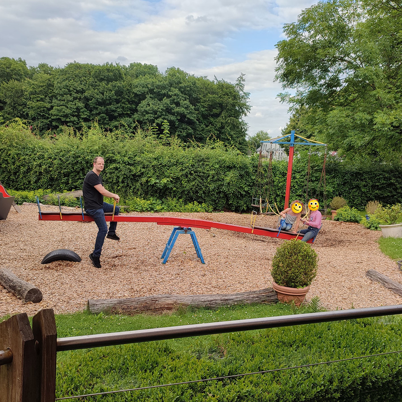 ein Erwachsener sitzt mit zwei Kindern auf einer roten Wippe auf einem Spielplatz